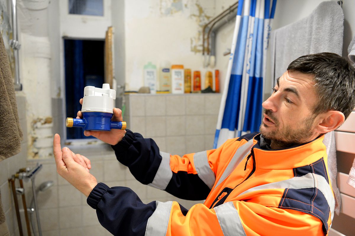 Un agent du service des eaux avec un équipement d'intervention montre un élément de robinetterie. Il effectue des travaux dans une salle de bain.  