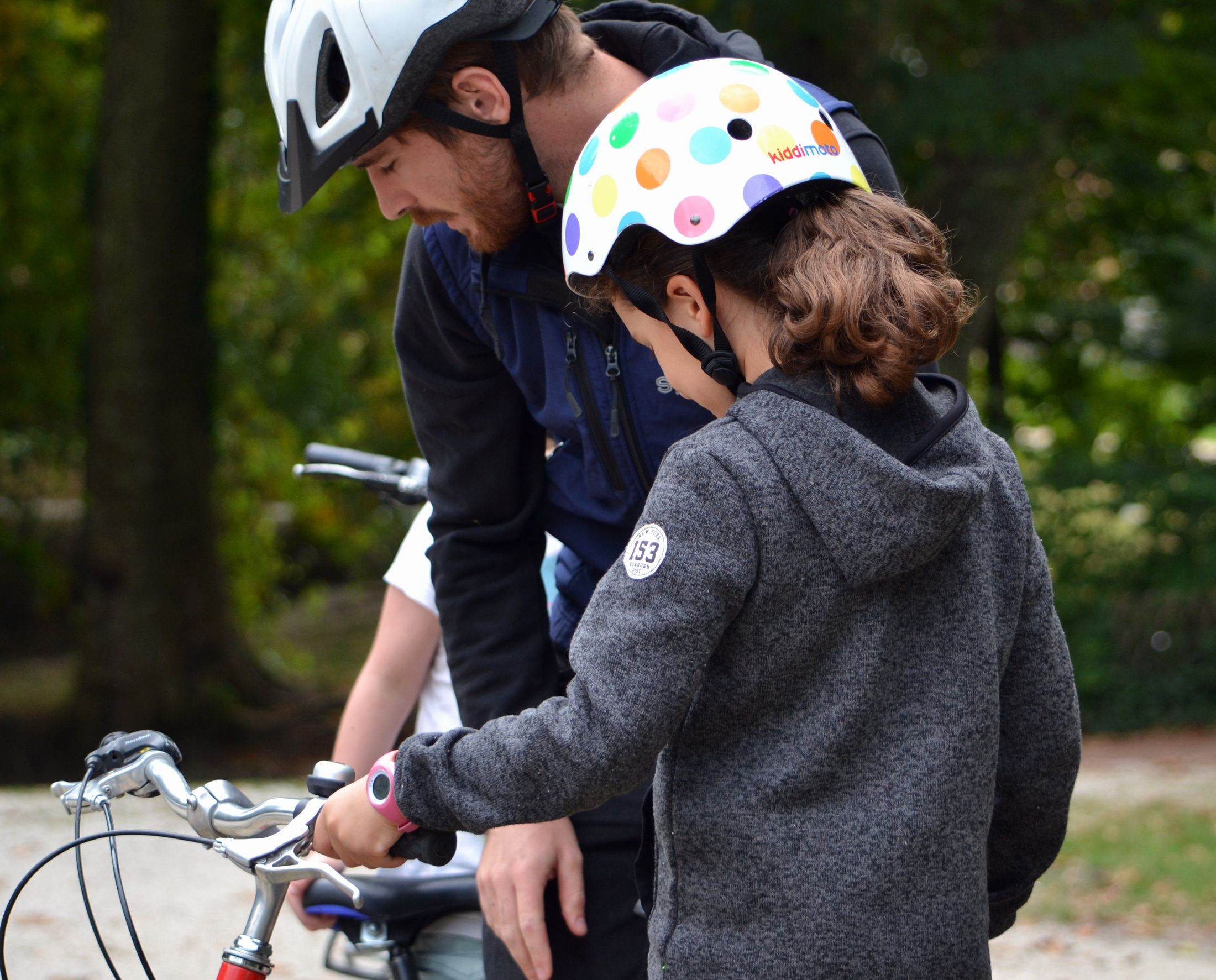 une petite fille de dos regarde l'éducateur vélo faire des réglages sur son vélo