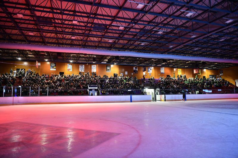 Patinoire de Grand Chambéry, la lumière est tamisée avec des tons rosés, la glace est vide et les tribunes sont remplies
