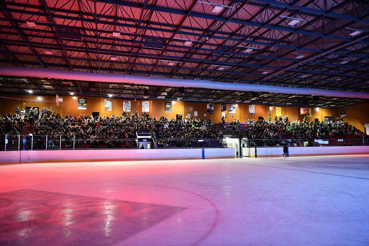 Patinoire de Grand Chambéry, la lumière est tamisée avec des tons rosés, la glace est vide et les tribunes sont remplies