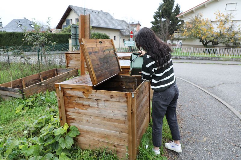Une personne dépose des déchets dans un composteur.