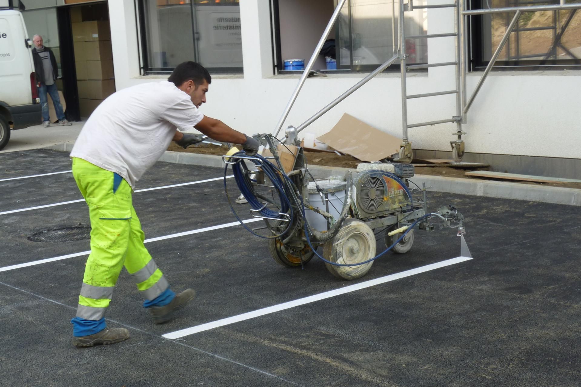 Sur un parking, un ouvrier utilise une machine pour faire le marquage au sol blanc pour les places de parking.