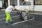 Sur un parking, un ouvrier utilise une machine pour faire le marquage au sol blanc pour les places de parking.