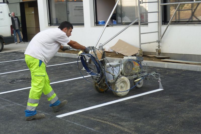 Sur un parking, un ouvrier utilise une machine pour faire le marquage au sol blanc pour les places de parking.