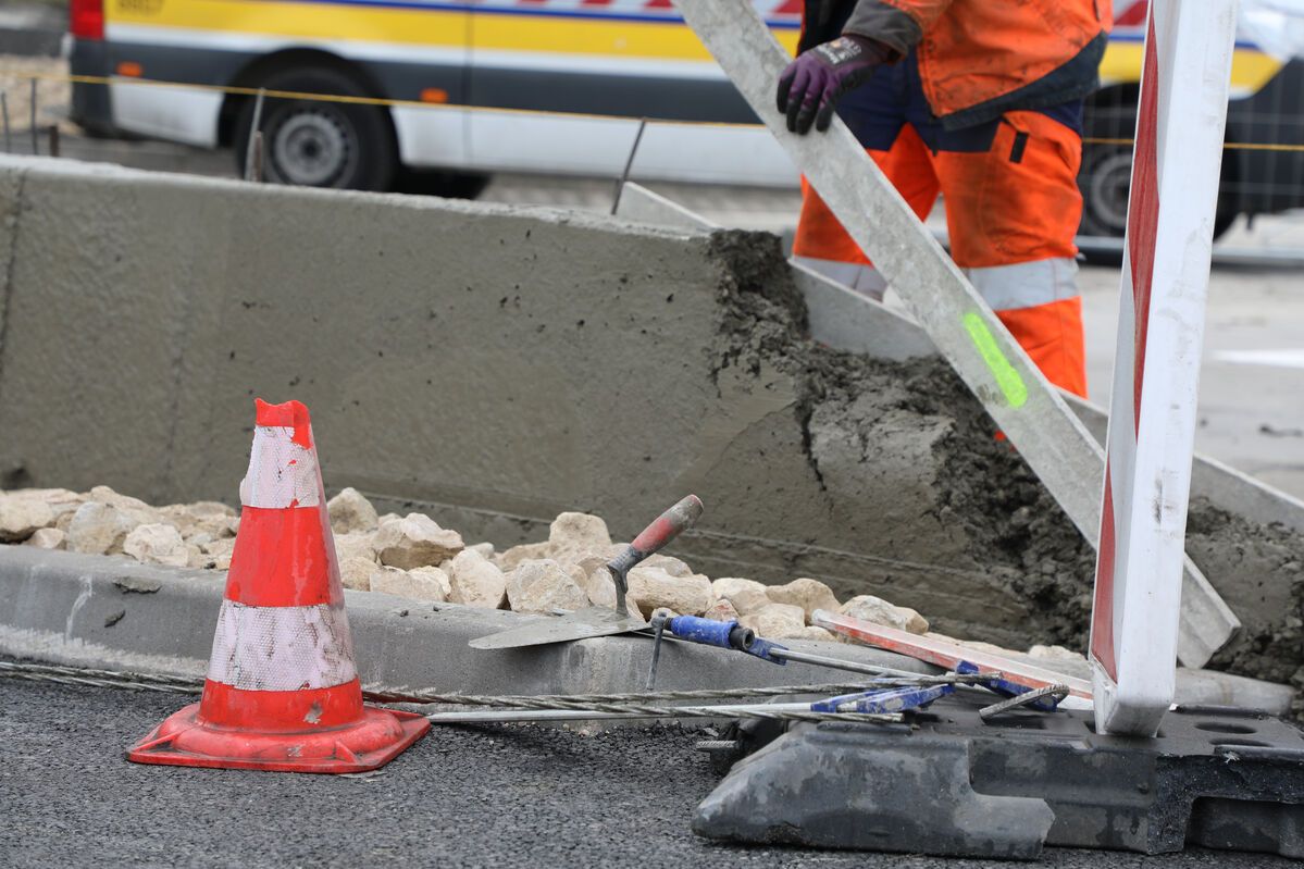 Un cône de chantier et des outils au niveau d'un muret. 