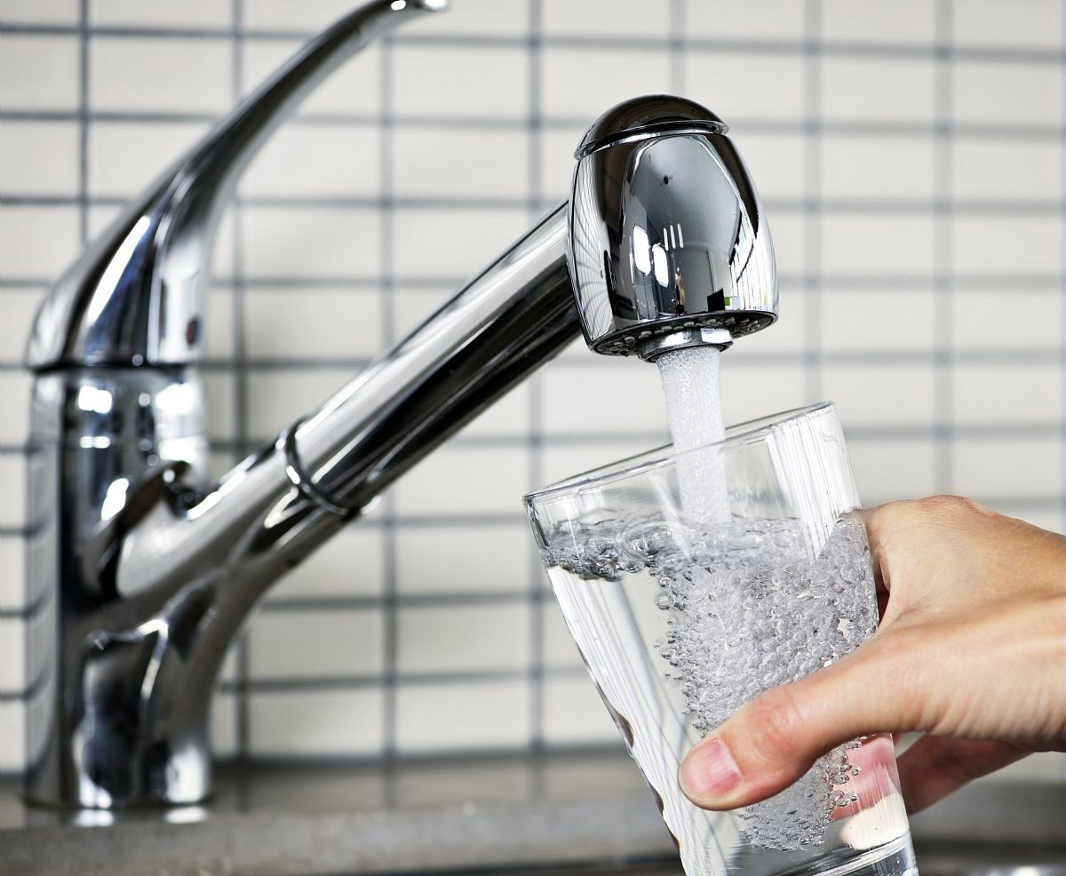 Une personne verse de l’eau du robinet dans un verre transparent.