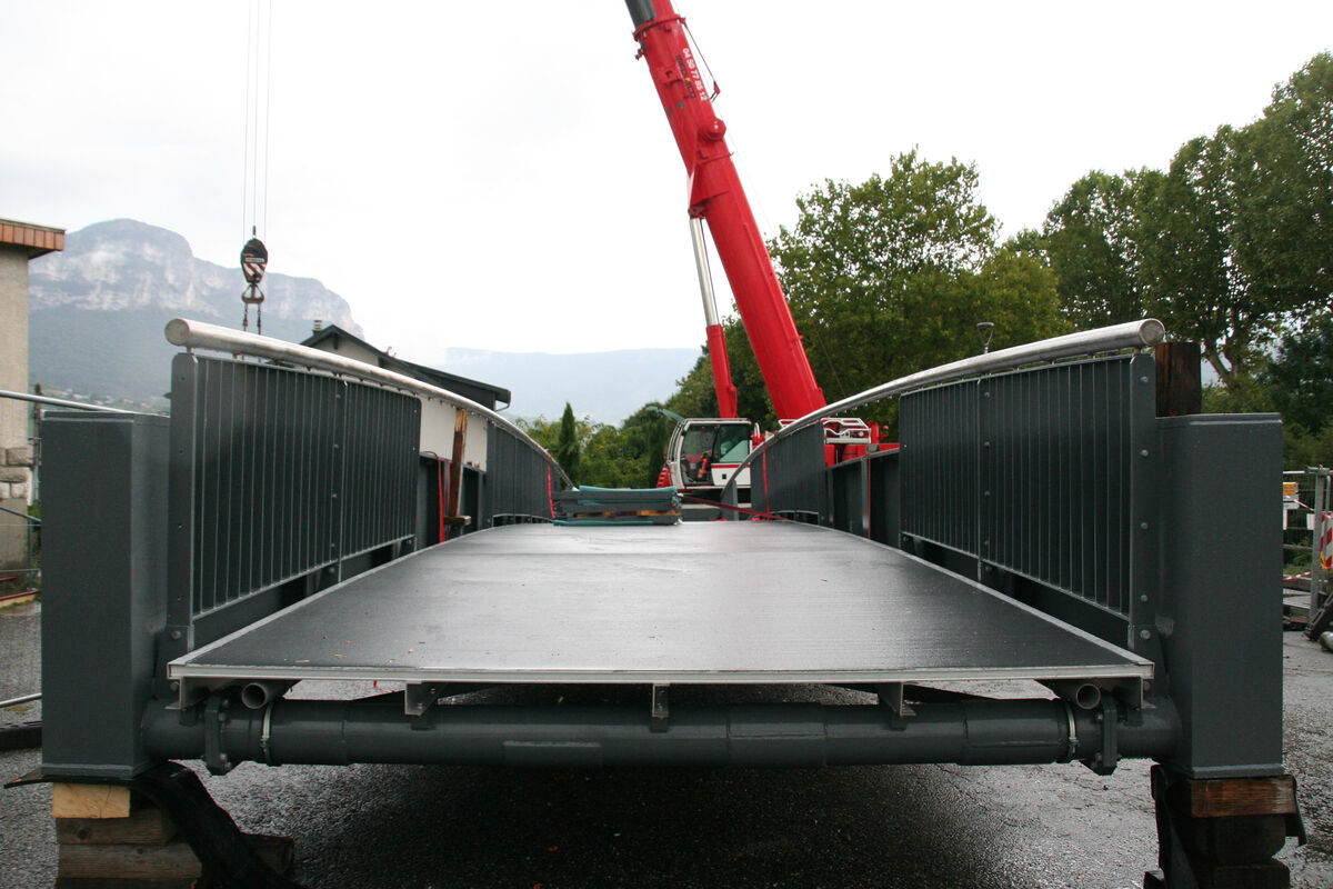 Une grue soulève une passerelle piétonne. 