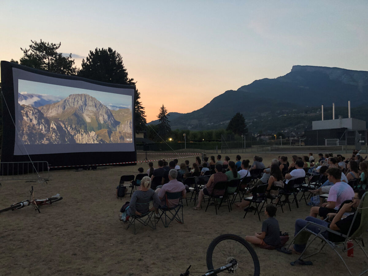 Dans un champs, des personnes regardent un film sur un grand écran