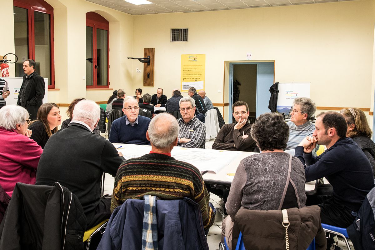 Des personnes assisent autour d'une table dans une salle municipale discutent