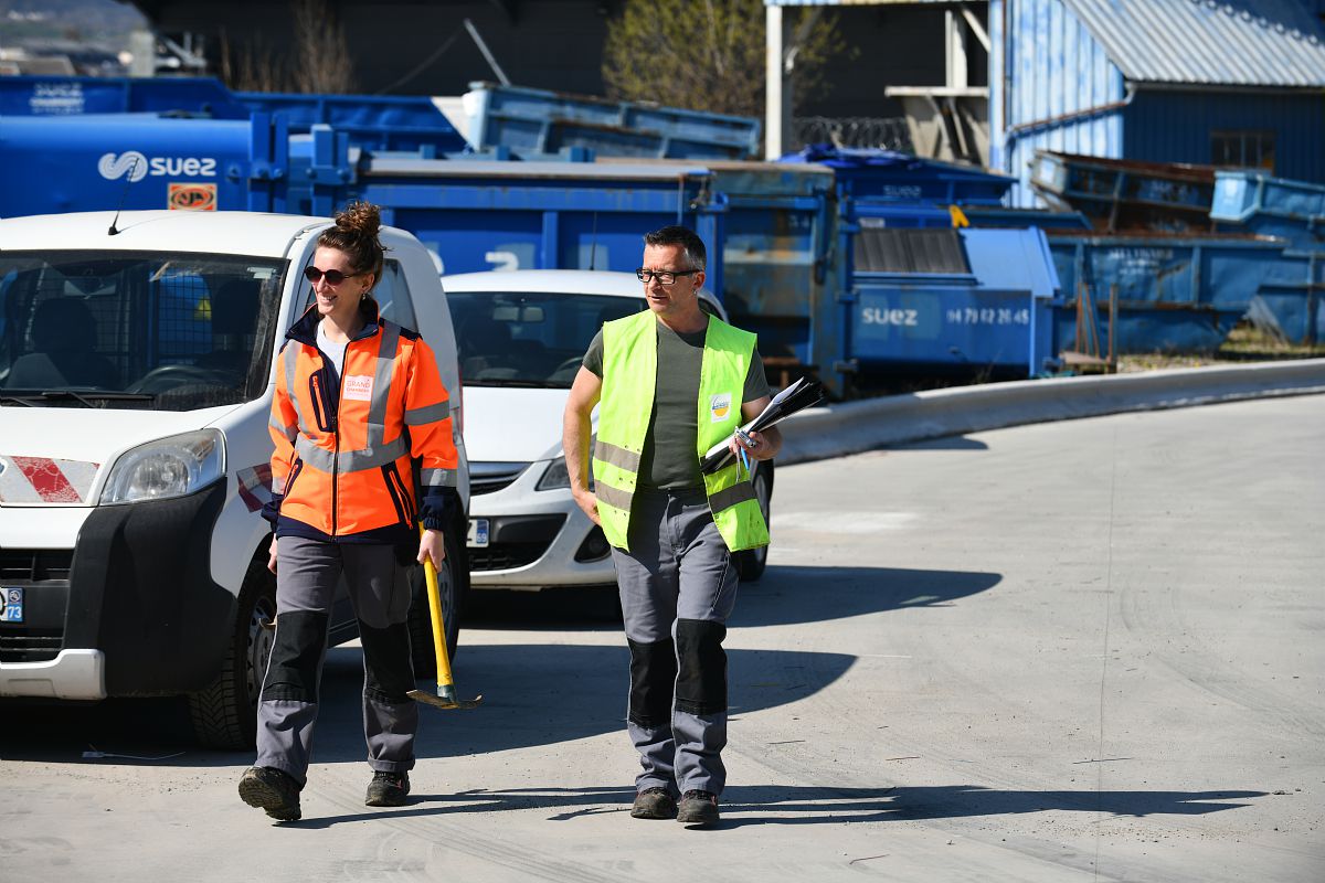 Deux techniciens marchent sur un parking avec des outils.