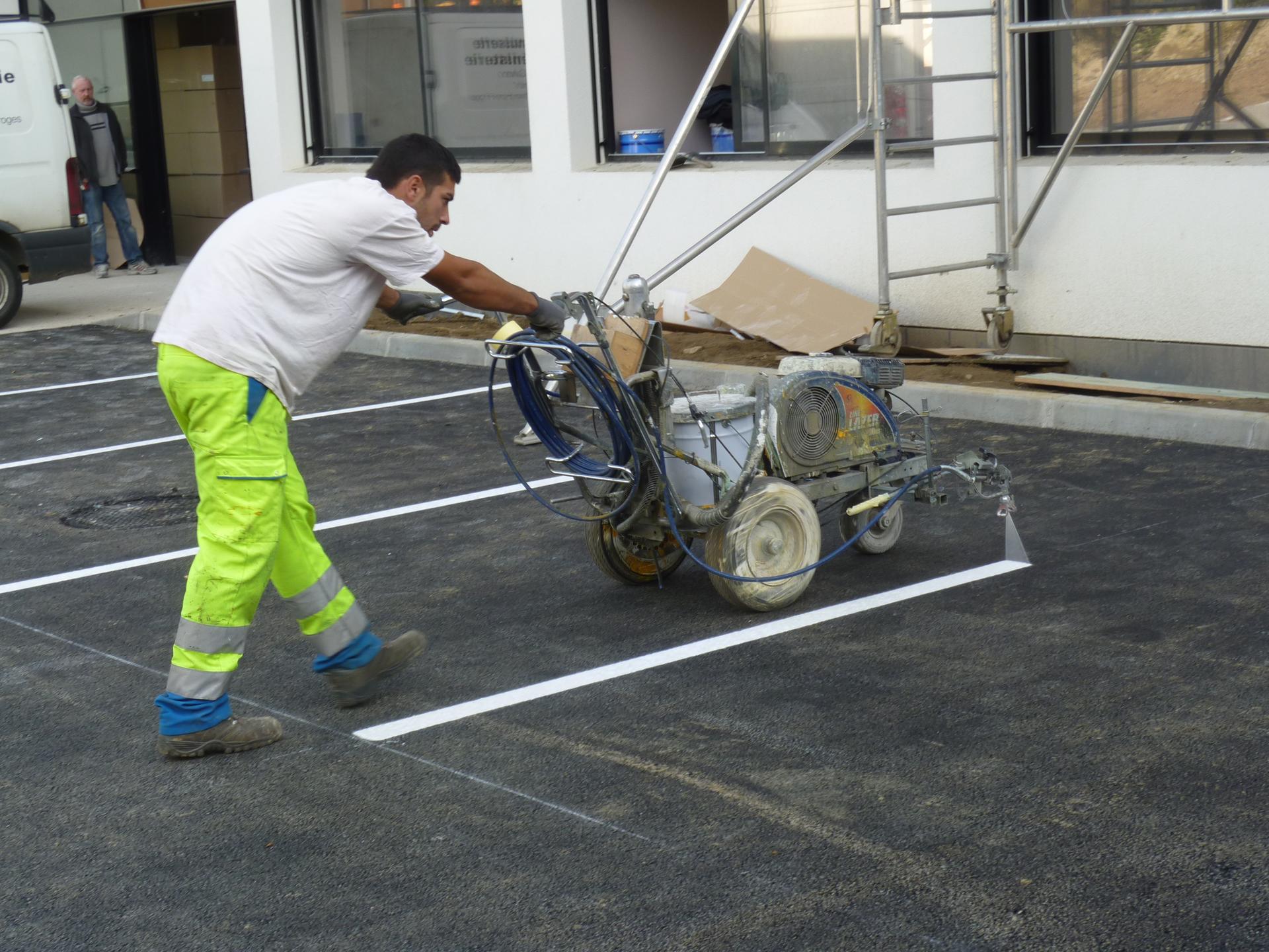 Sur un parking, un ouvrier utilise une machine pour faire le marquage au sol blanc pour les places de parking.