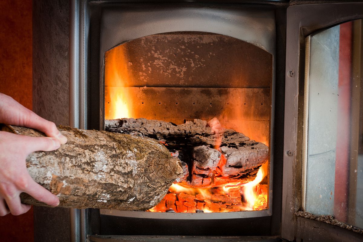 Deux mains mettent une bûche dans un poêle à bois.