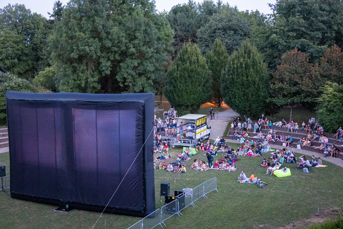 Des personnes assisent dans l'herbe regardent un film en extérieur à la tombée de la nuit