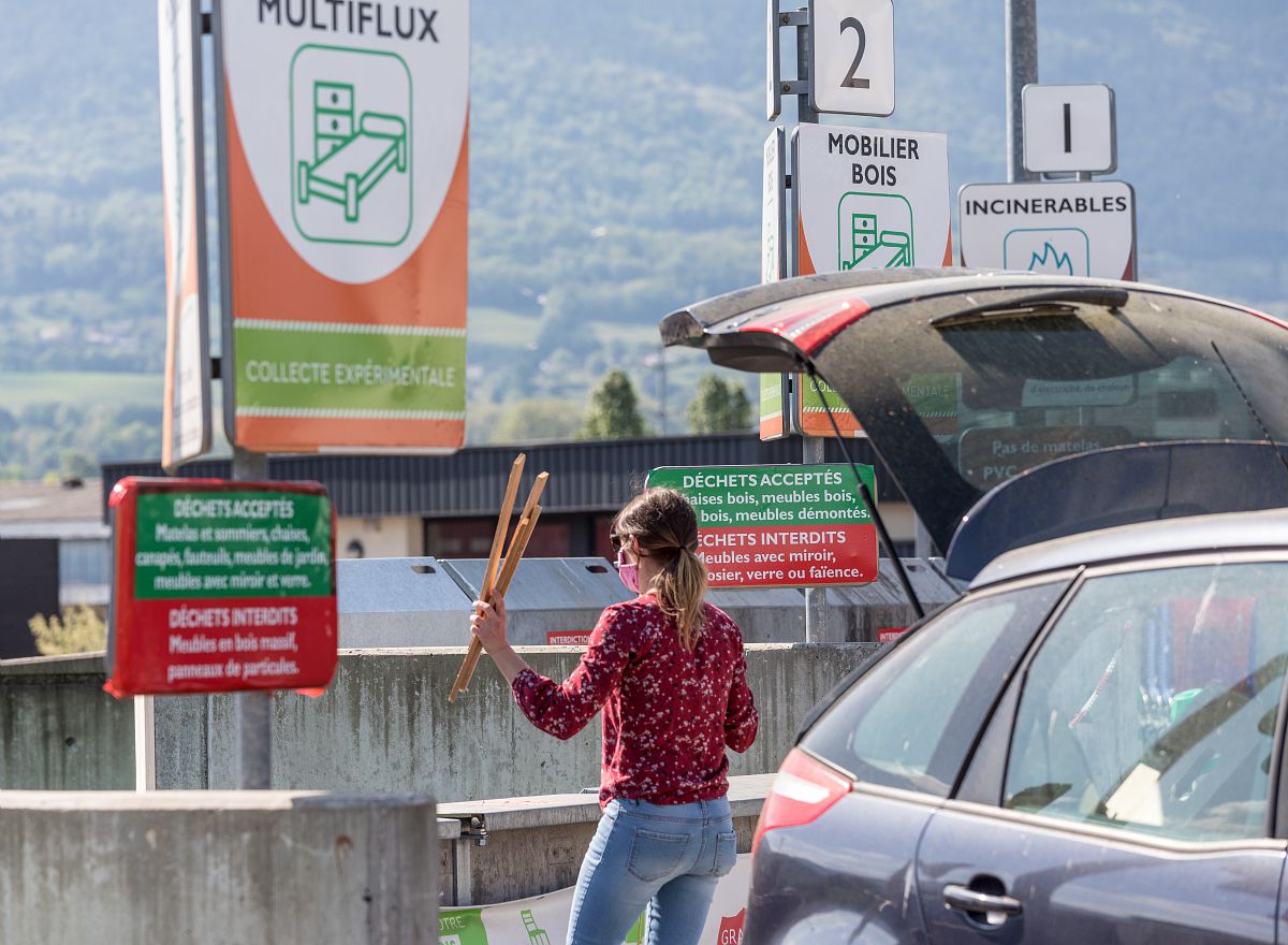 Une jeune femme dépose des déchets dans la benne d'une déchetterie. Elle est à côté de sa voiture qui semble contenir encore des déchets dedans