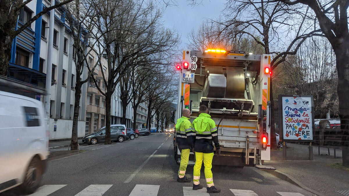 Deux collecteurs des poubelles sont à l'arrière d'un camion de collecte en pleine rue, tôt le matin, pour collecter les ordures ménagères