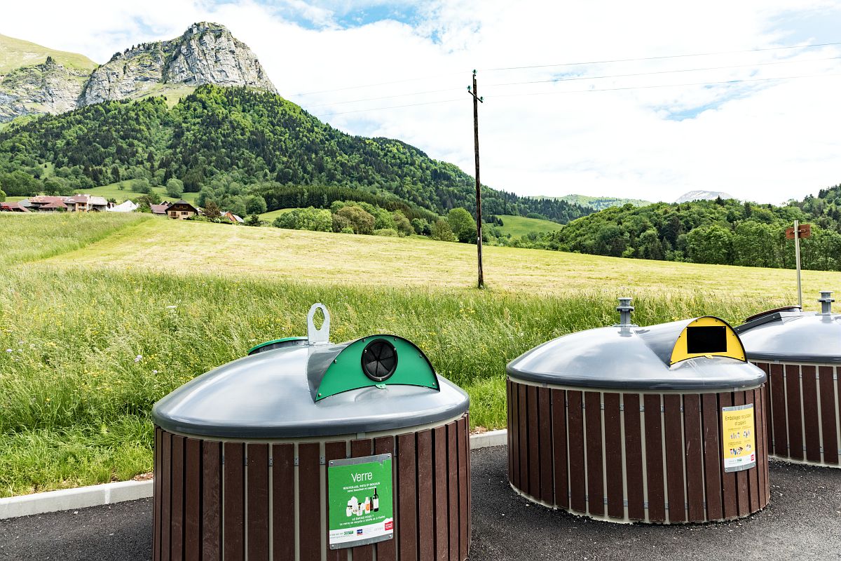 Des bacs pour y déposer les déchets recyclables au bord d'un champ. En arrière-plan il est possible de distinguer des montagnes