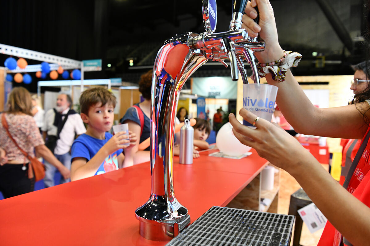 Une main appuie sur une tireuse à eau pour remplir un verre d'eau.